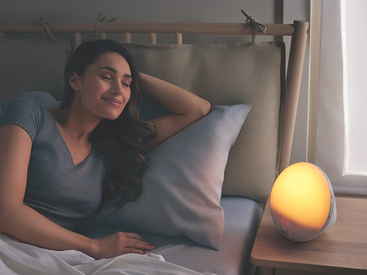 Exact Philips SmartSleep HF3520/60 glowing on a bedside table beside a waking person